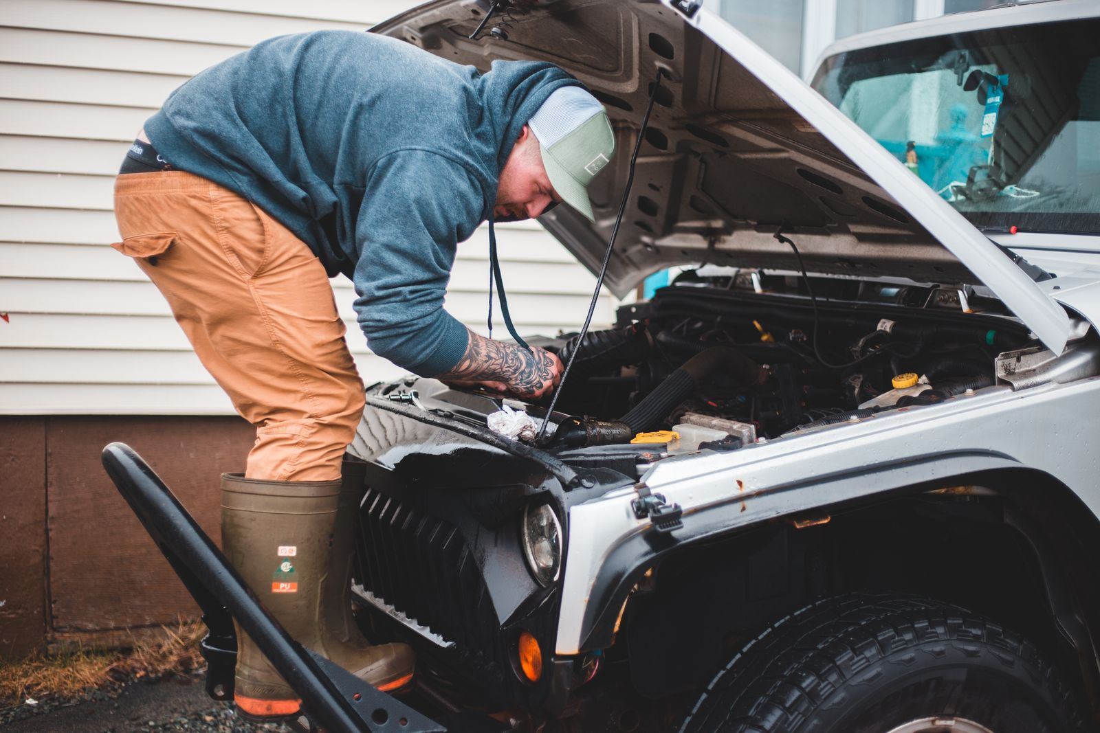A car owner in their driveway working underneath the hood of their own vehicle